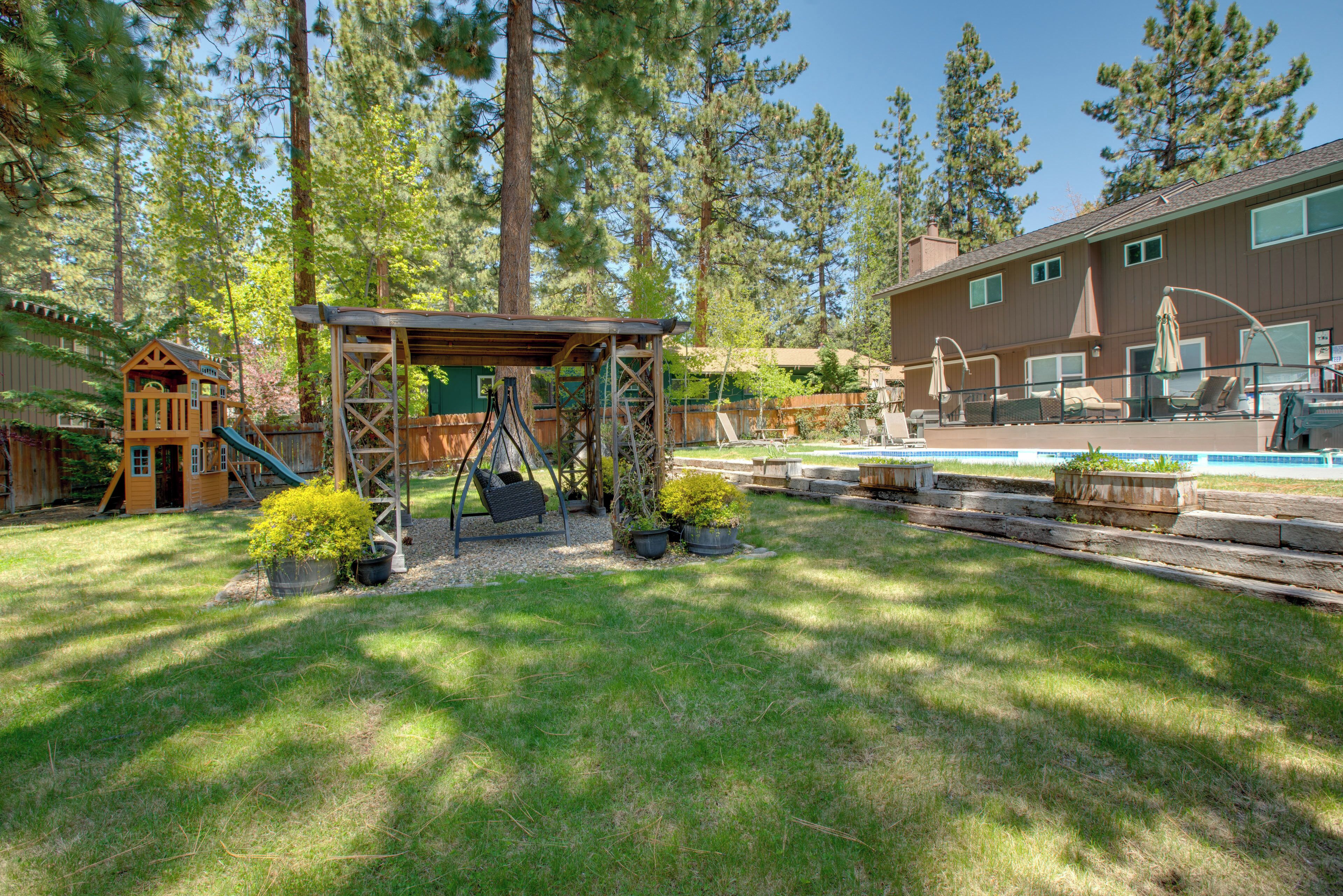 A backyard with a swing set, a small playhouse, and a pool area.