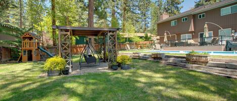 A backyard with a swing set, a small playhouse, and a pool area.