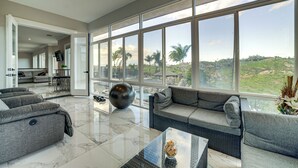 A spacious living room with a large window, a gray sofa, a coffee table, and a modern decorative bowl.