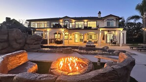 A large house with a fire pit in the front yard, a balcony, and a covered patio area.
