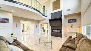 A spacious living area with a curved staircase, a large sectional sofa, a glass coffee table, and a flat-screen TV mounted on the wall.
