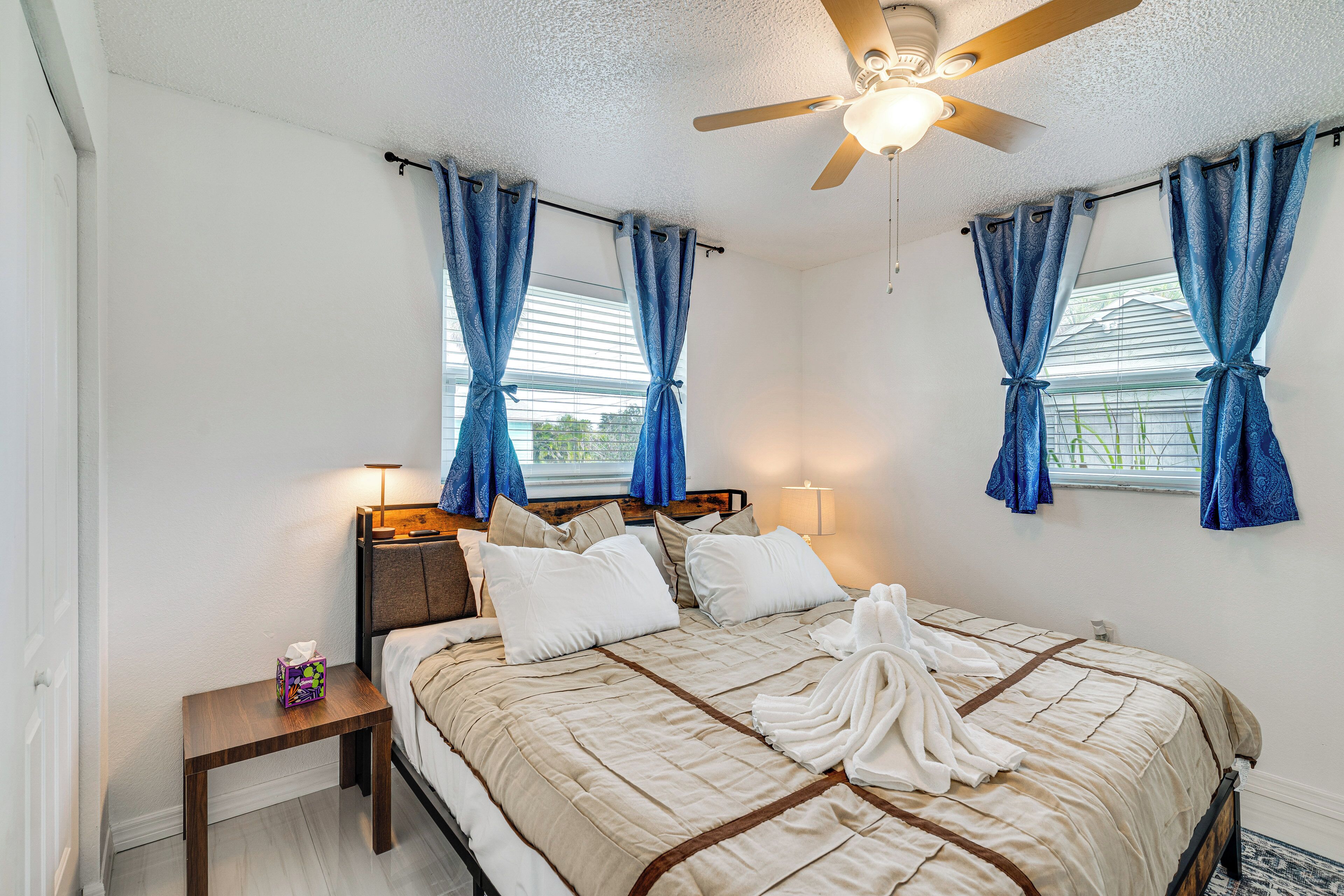 A neatly made bed with a beige and brown striped bedspread, two bedside lamps, and a nightstand with a tissue box.