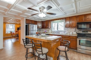 A spacious kitchen with wooden cabinets, a large island with bar stools, a built-in oven, and a ceiling fan. - Mtn-view Balcony! Convenient Apt Near Jim Thorpe (Nesquehoning)