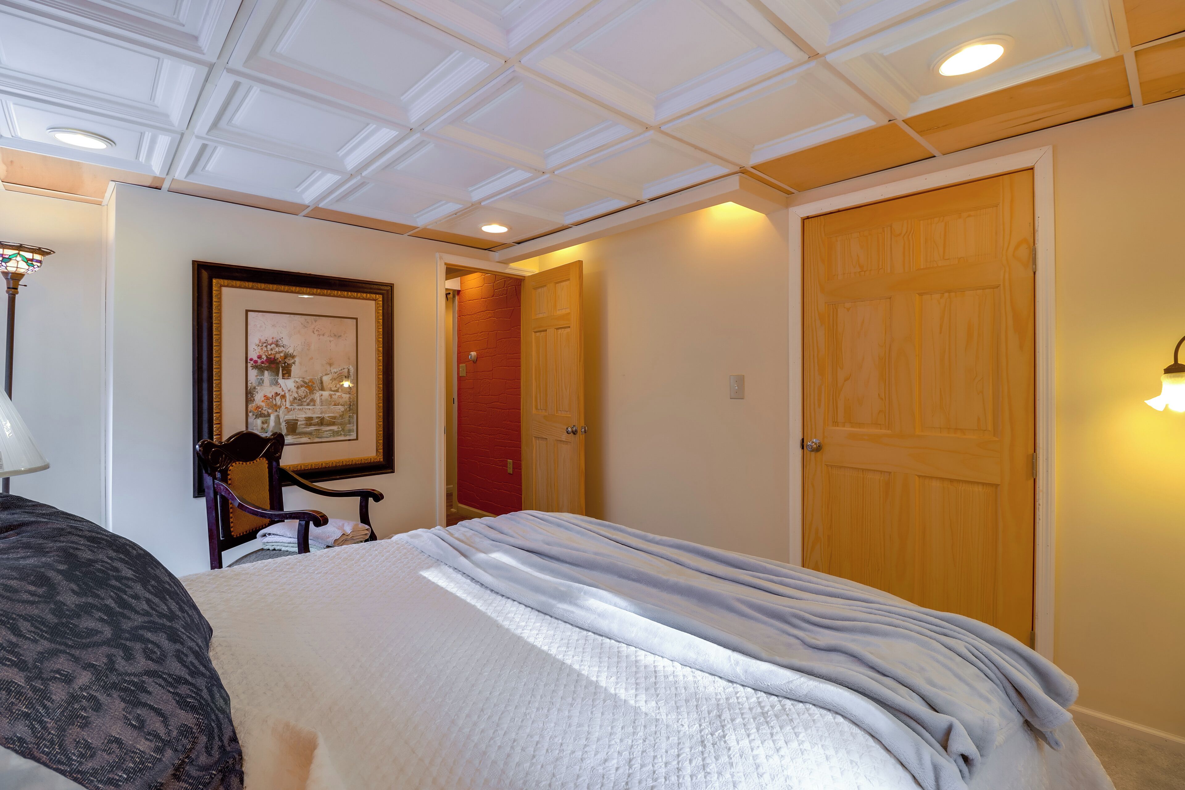Une chambre d’hôtel avec un lit, une chaise, un tableau encadré au mur et une porte en bois.