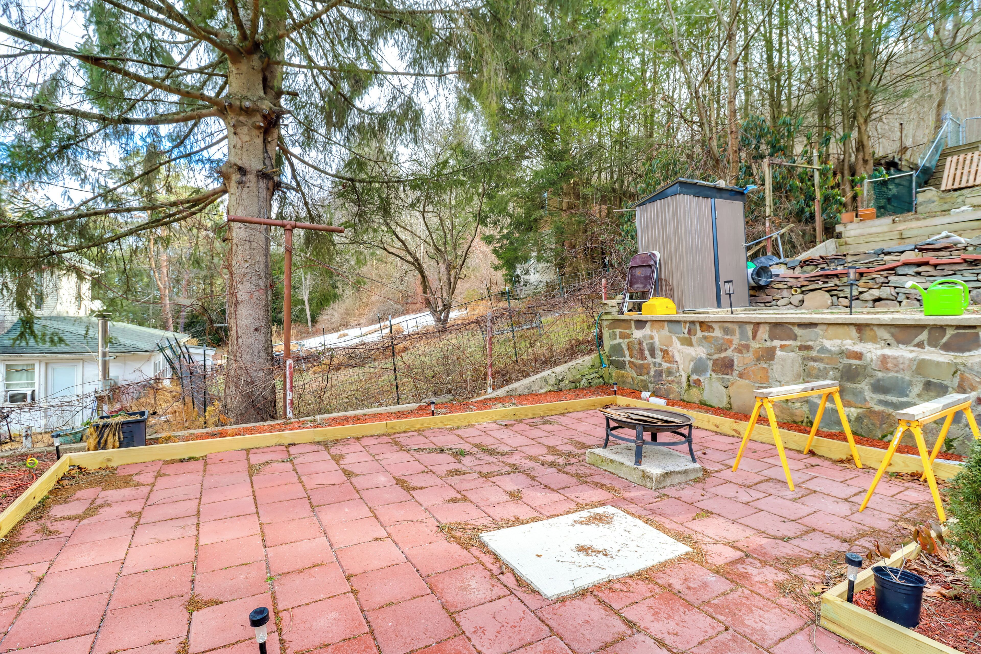 Un patio trasero con un suelo empedrado, un banco de madera, un cobertizo pequeño y un árbol.