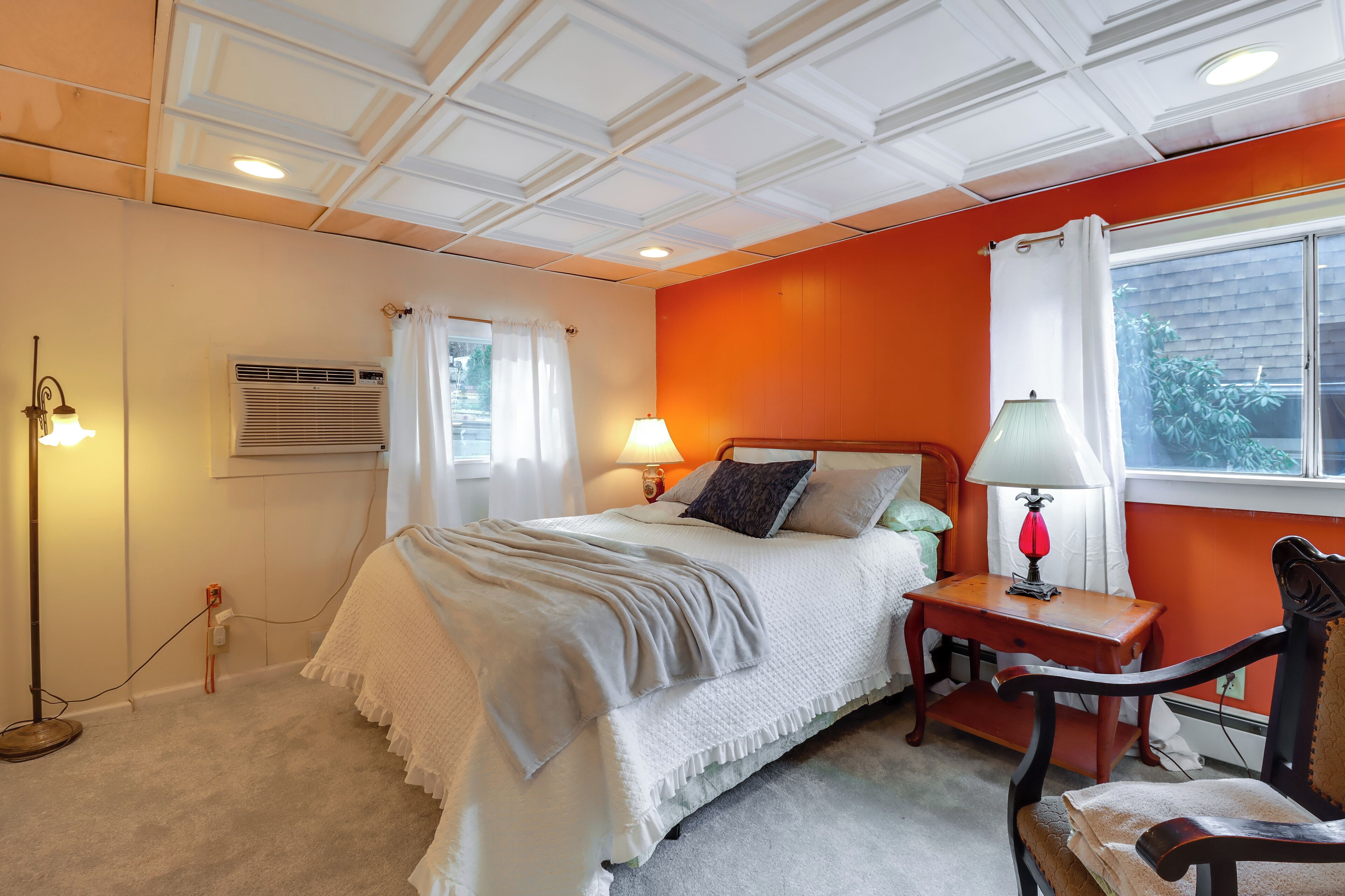 A bedroom with a bed, bedside lamps, a chair, and a window with curtains.