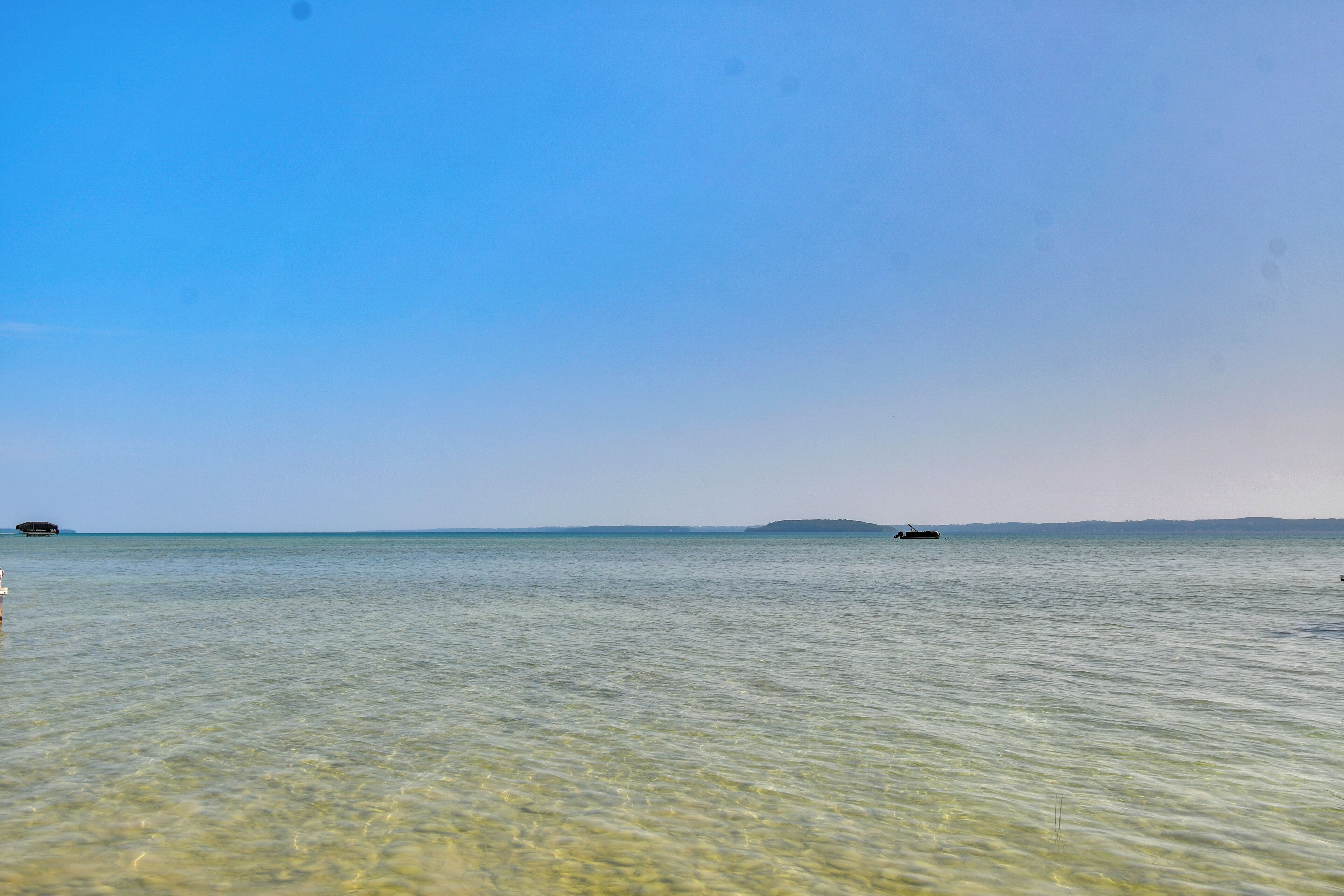 A clear view of a calm sea with a distant landmass and a boat.
