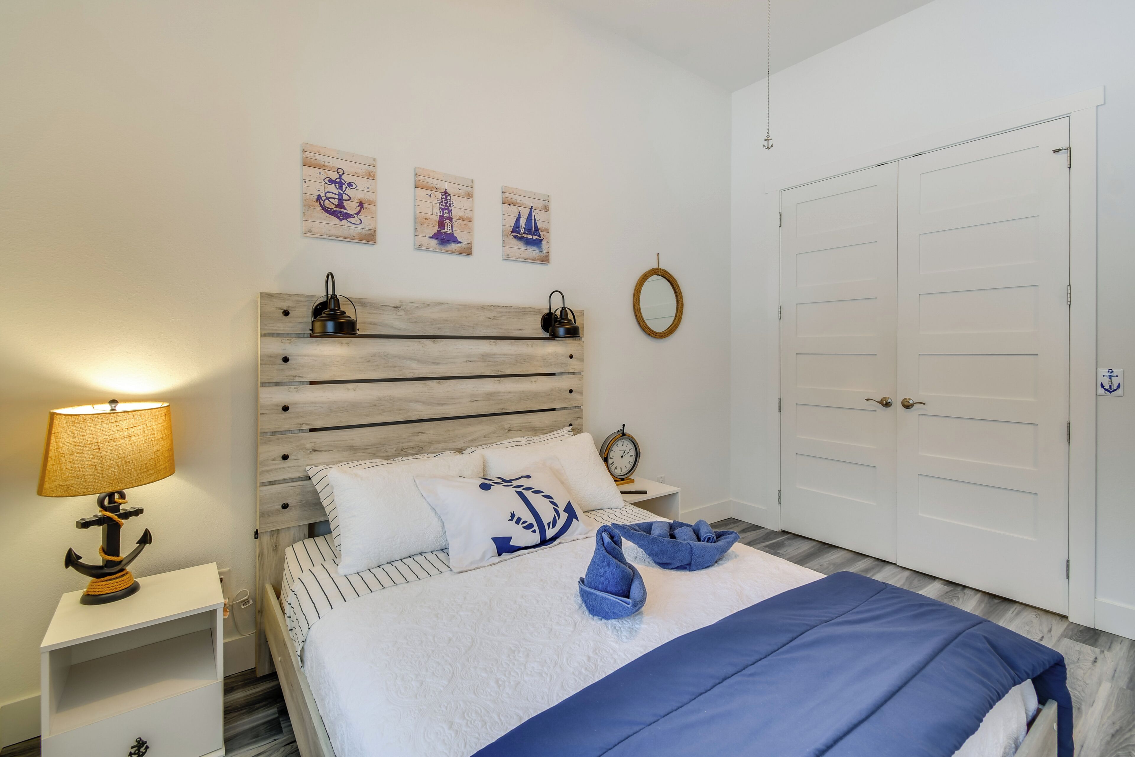 A neatly arranged bedroom with a wooden headboard, a bed with striped bedding, a bedside table with a lamp, and a wall-mounted mirror.