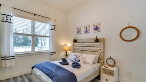 Ein Schlafzimmer mit einem Bett, einem Nachttisch mit Lampe, einem runden Spiegel und Wandkunst im maritimen Stil.