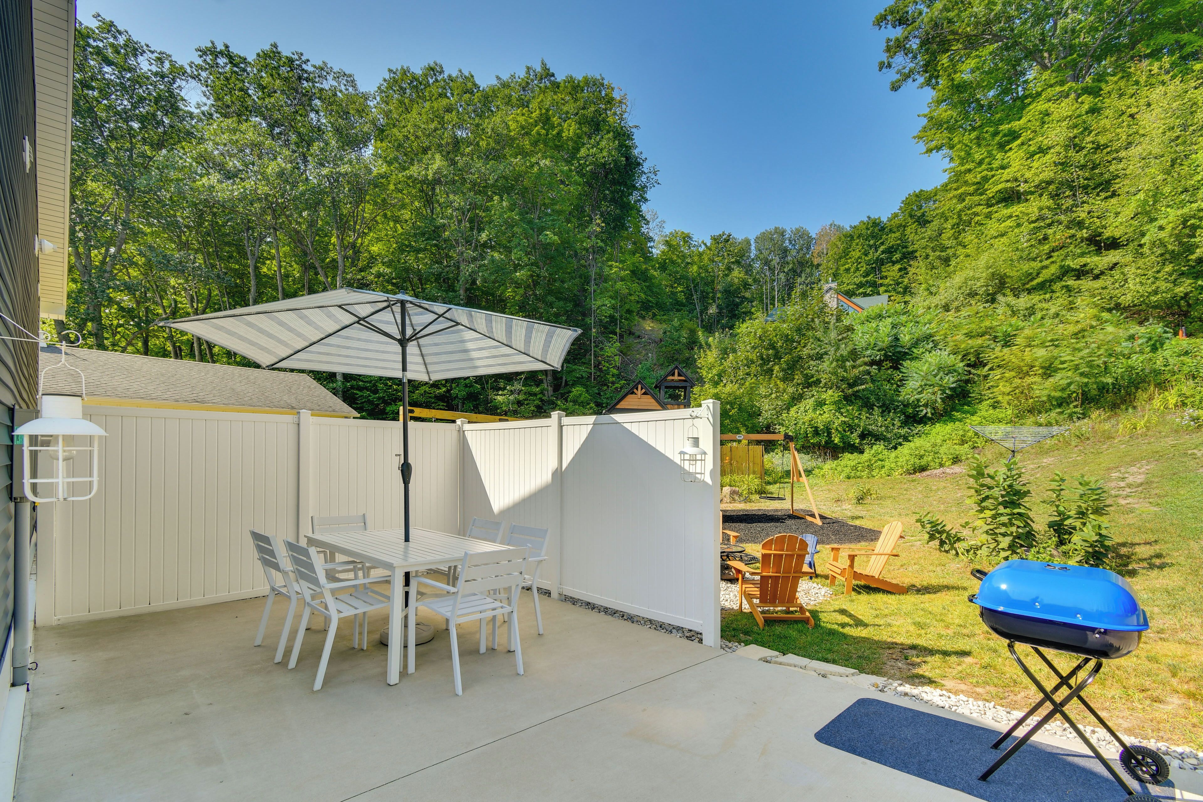 Une terrasse avec une table et des chaises, un barbecue et une clôture blanche.