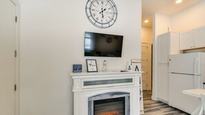 Eine moderne Küche mit weißen Schränken, einem eingebauten Kamin, einem Wand-Fernseher und einer Uhr.
