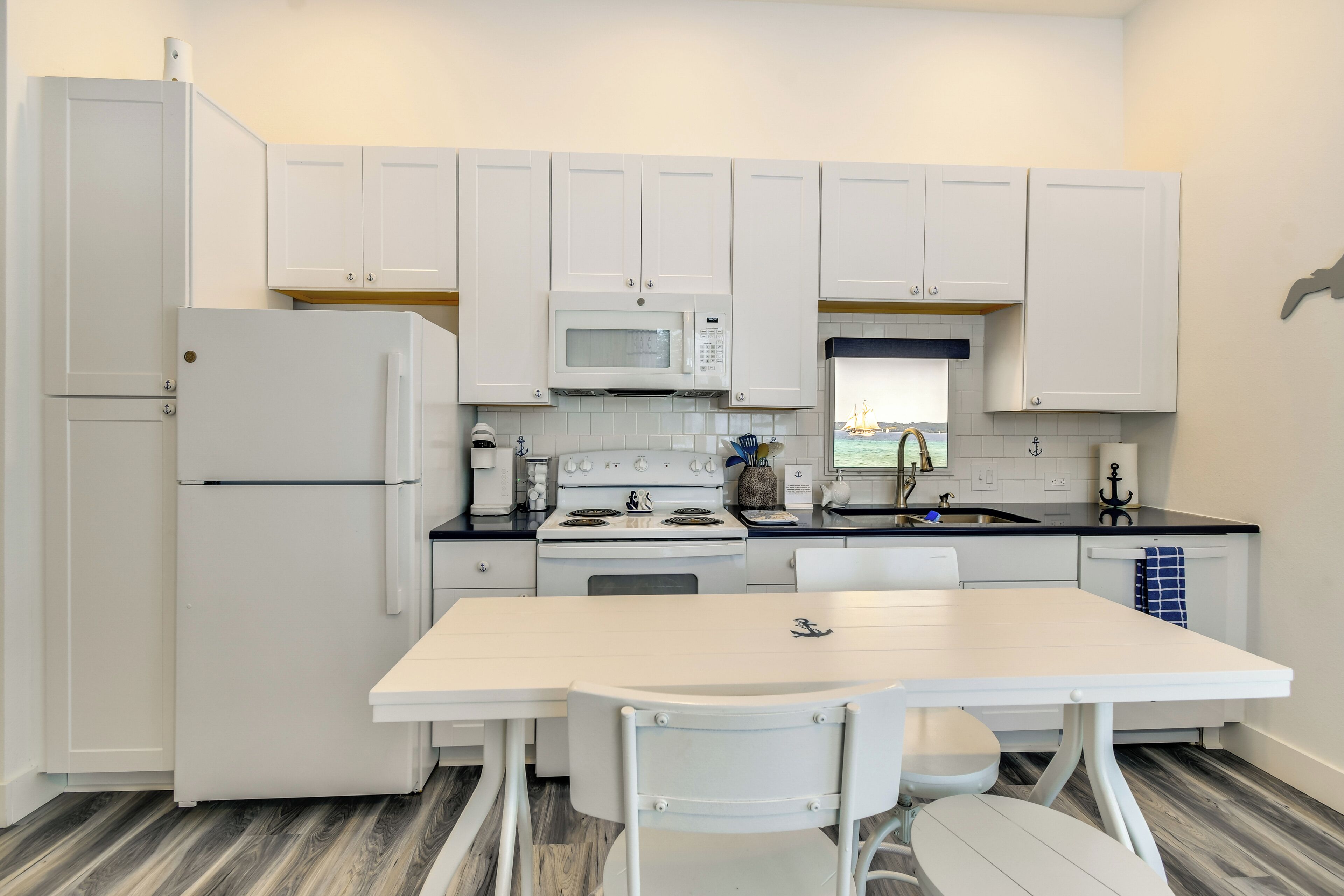 A compact kitchen with white cabinetry, a refrigerator, a microwave, an oven, and a sink.