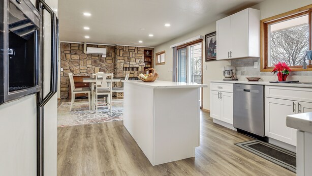 A modern kitchen with a central island, white cabinetry, a stone accent wall, and a view of the outdoors through a window. - 2 Mi to Golf Course! Family Home in Pueblo West (Pueblo)