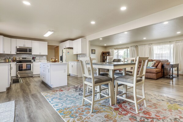 A modern kitchen with white cabinets, a microwave, and an oven. There is a dining area with a table and chairs, and a living room with a sofa and a coffee table. - 2 Mi to Golf Course! Family Home in Pueblo West (Pueblo)