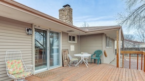 A covered deck with a wooden floor, a stone chimney, a glass door leading to a patio, and a small table with chairs. - 2 Mi to Golf Course! Family Home in Pueblo West (Pueblo)