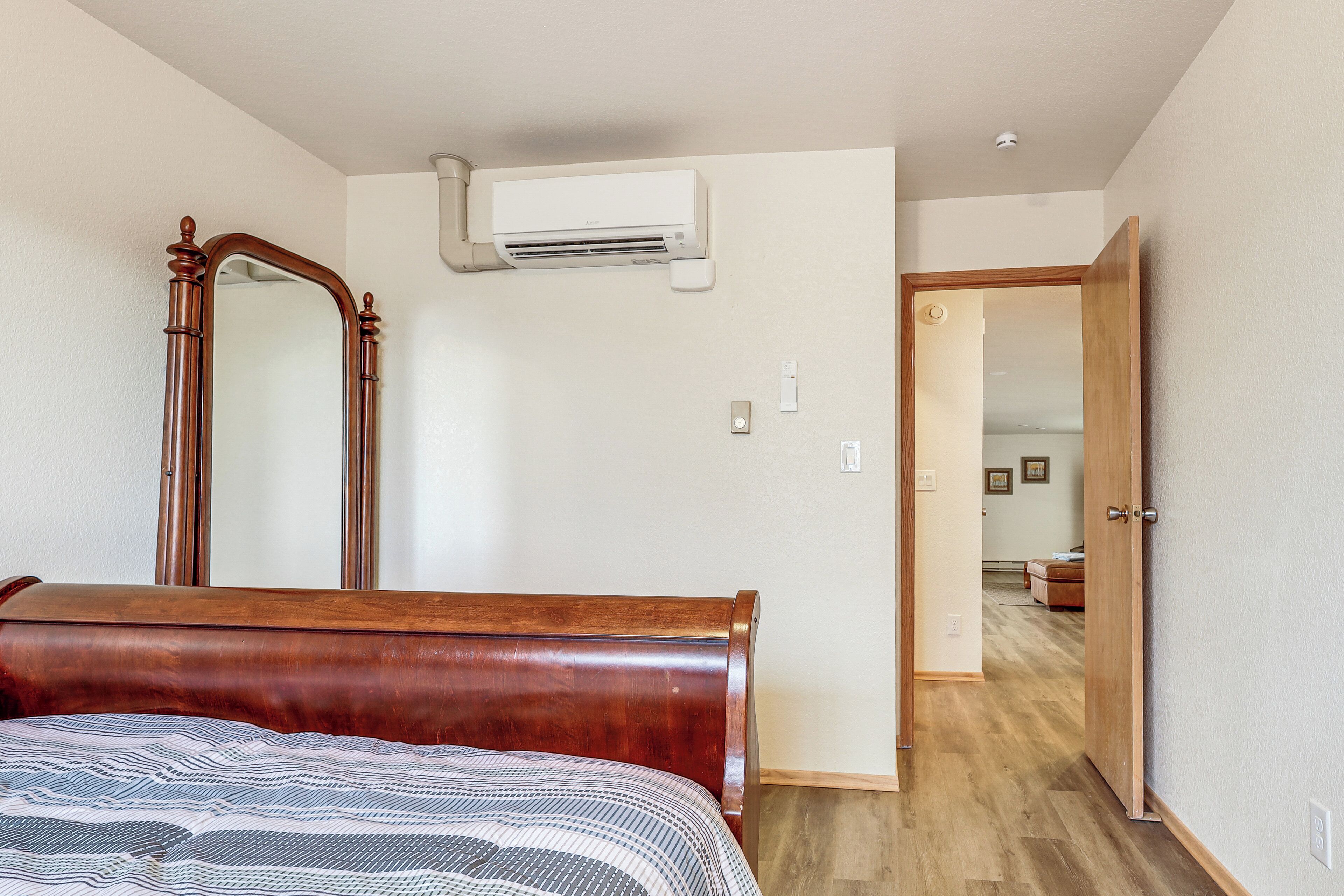 A bedroom with a wooden bed, a large mirror, and an air conditioning unit on the wall.