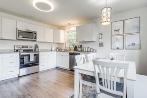 A modern kitchen with white cabinetry, stainless steel appliances, and a dining area with white furniture. - 1 Mi to Park Circle: Pet-friendly Home w/ Yard (North Charleston)