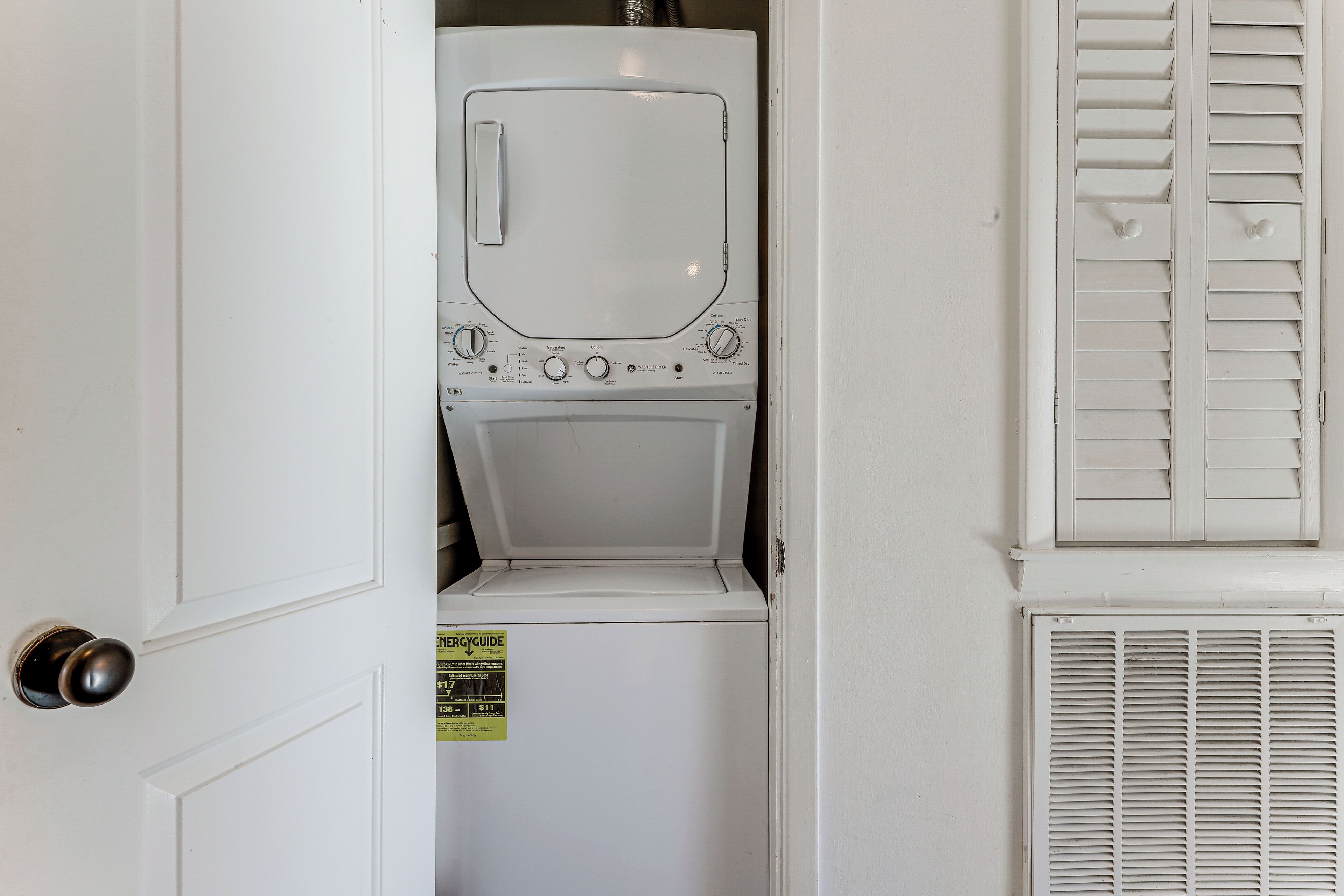 Máquina de lavar roupa branca numa lavanderia, com porta e ventilação.