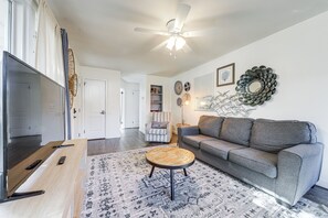 Ein Wohnzimmer mit grauem Sofa, einem runden Couchtisch, einem Fernseher und einem Deckenventilator.