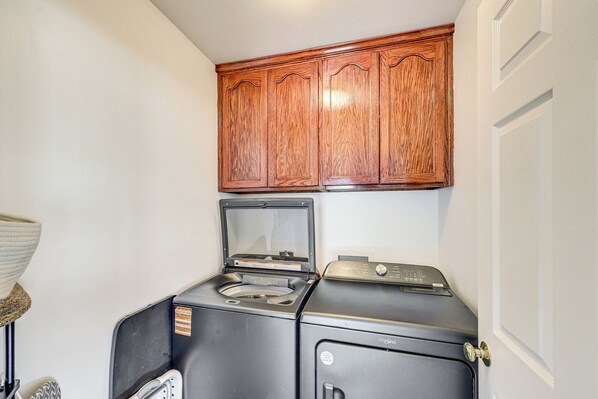 A compact laundry area with a washing machine and dryer, wooden cabinets above, and a door to the right.