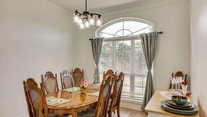 Comedor con mesa de madera, seis sillas, una araña y una ventana con cortinas.