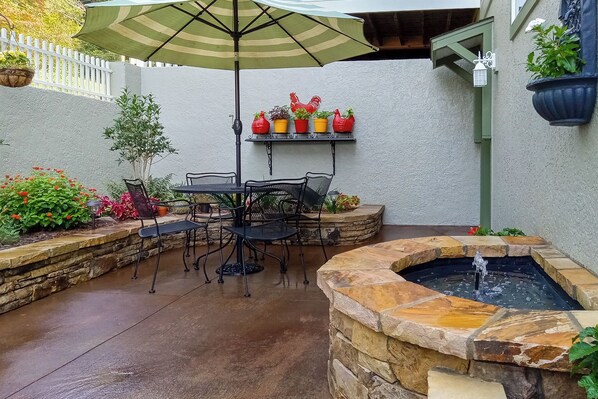 Une terrasse avec une table et des chaises, une fontaine en pierre et des plantes en pot.