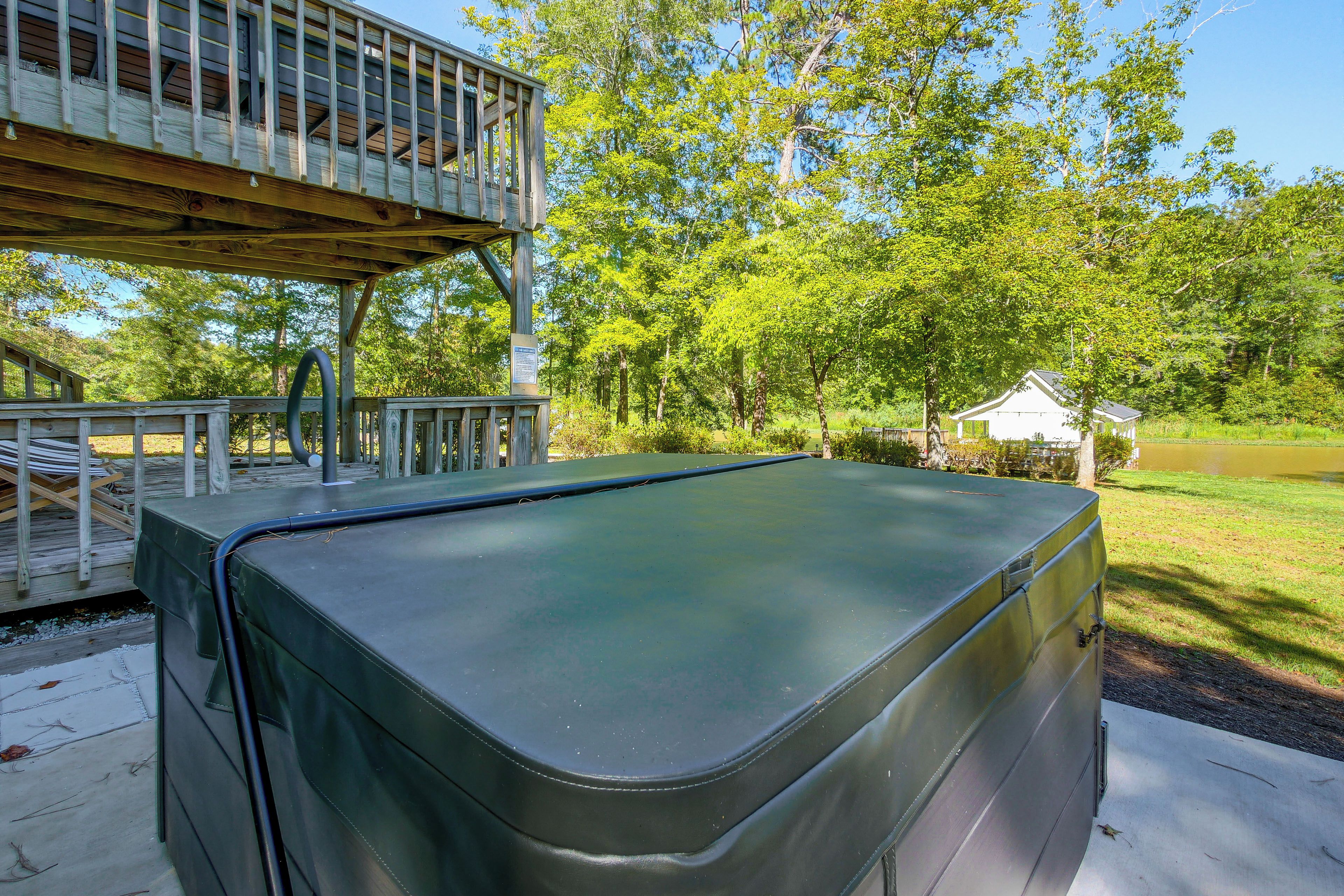 A hot tub with a wooden deck and a covered area, surrounded by trees and a small building.