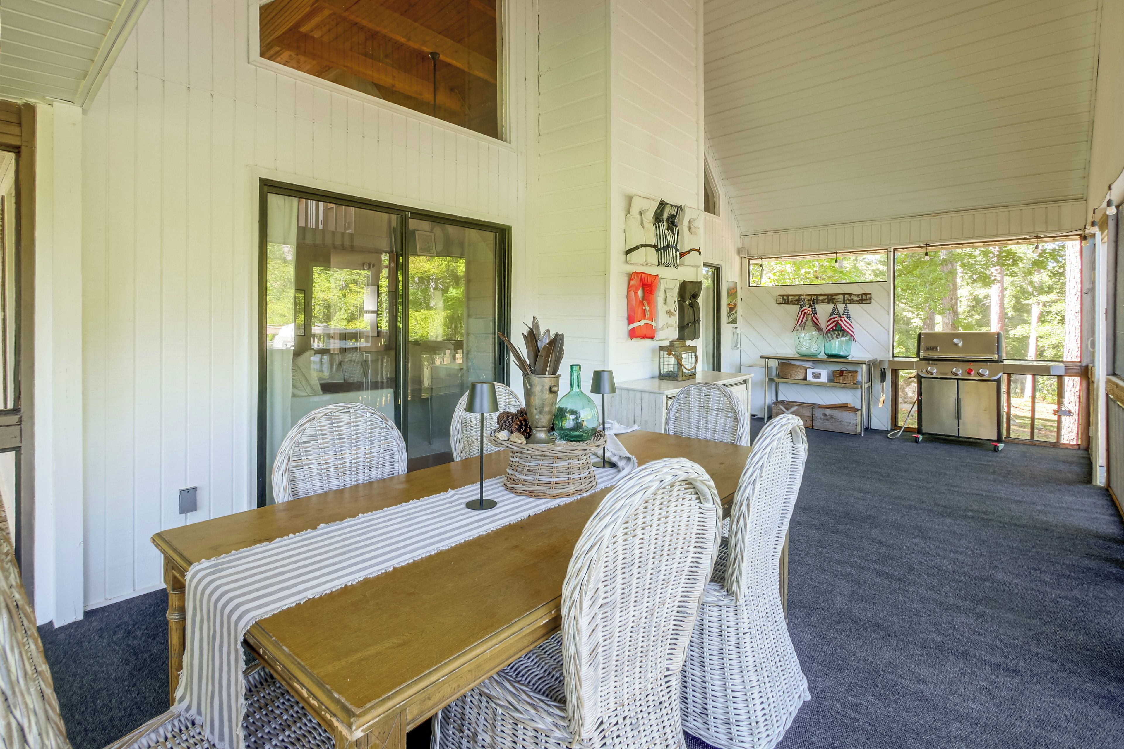 A dining area with a wooden table and wicker chairs, a glass door leading outside, and a kitchen area with a grill.