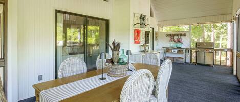 A dining area with a wooden table and wicker chairs, a glass door leading outside, and a kitchen area with a grill.