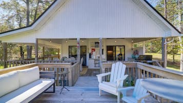 A covered deck with a white building, outdoor seating, and a grill area.