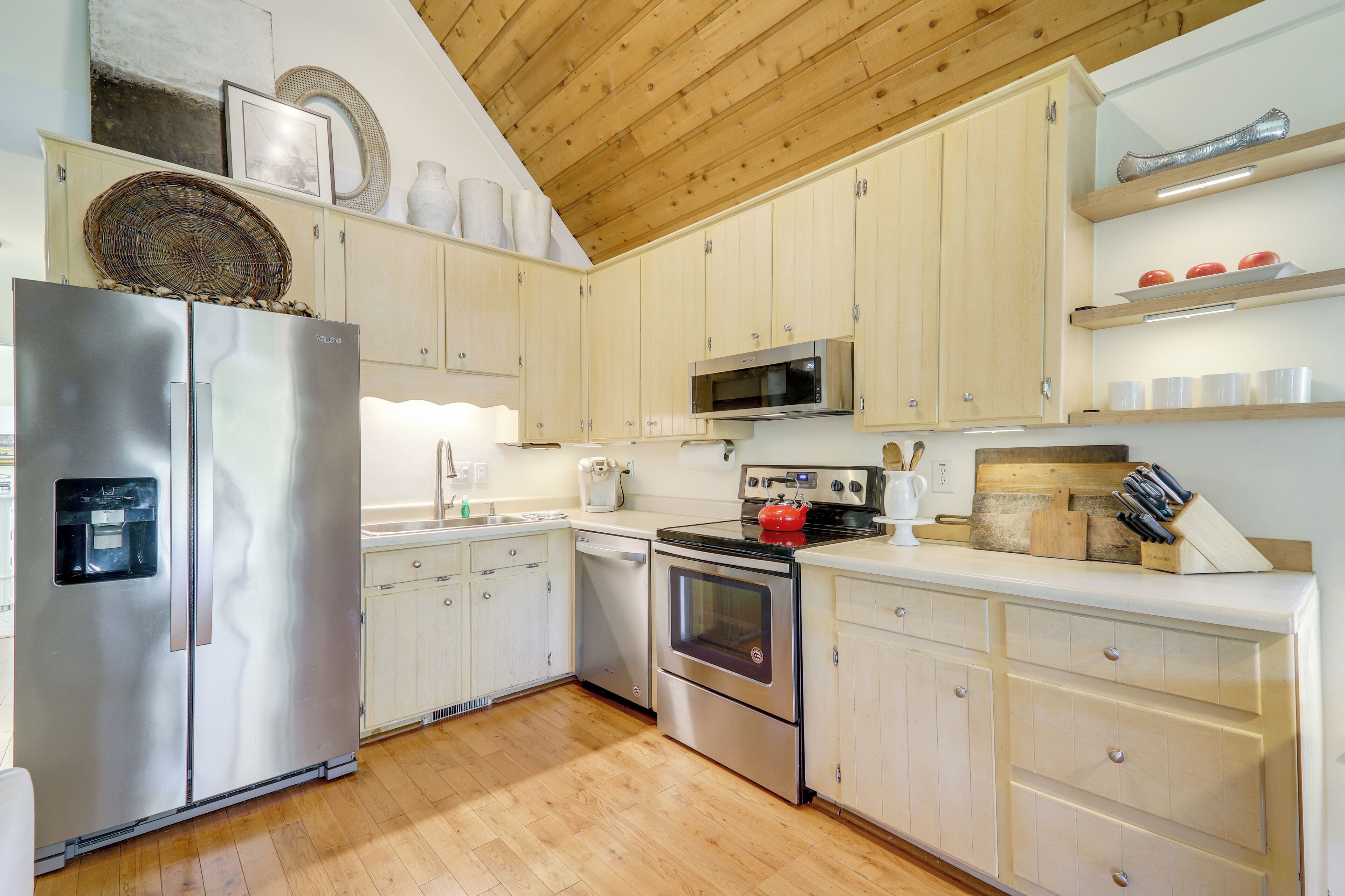 A modern kitchen with stainless steel appliances, wooden cabinets, and a wooden ceiling.