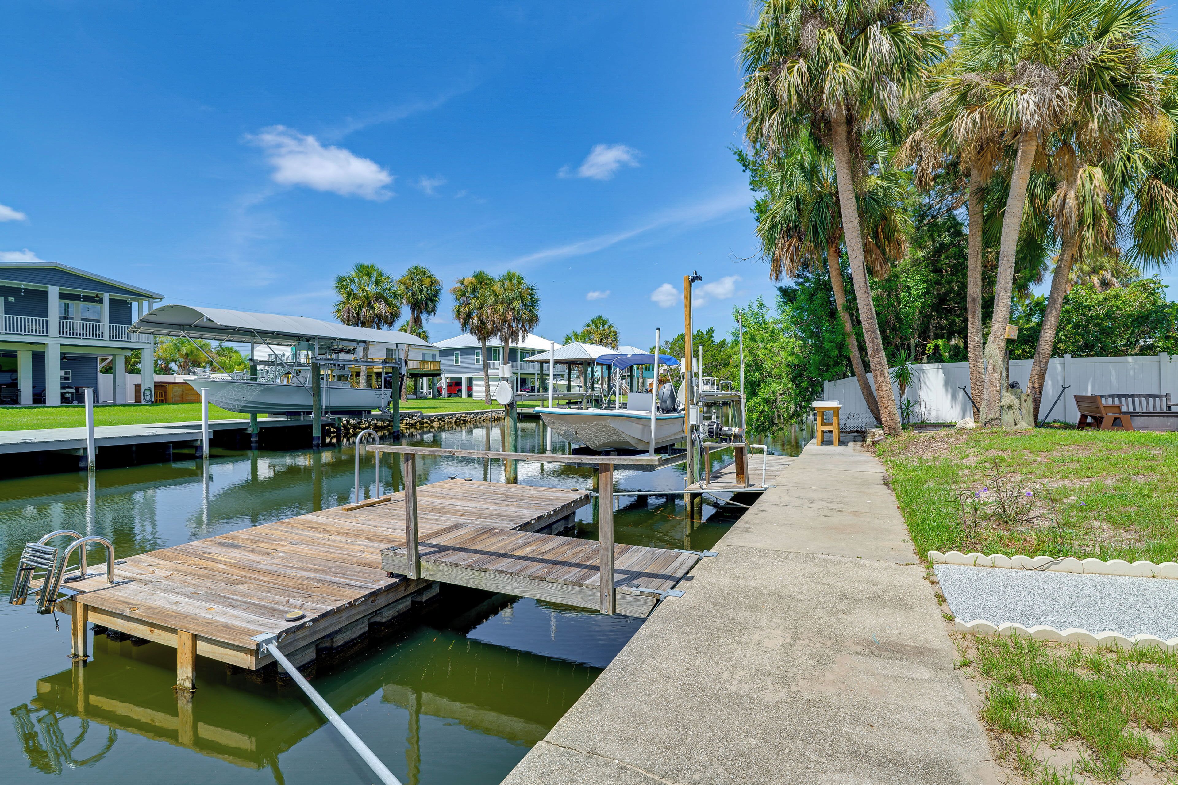 A marina with docked boats, a wooden pier, and a pathway leading to a building with a covered area.