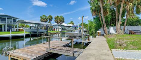 A marina with docked boats, a wooden pier, and a pathway leading to a building with a covered area.