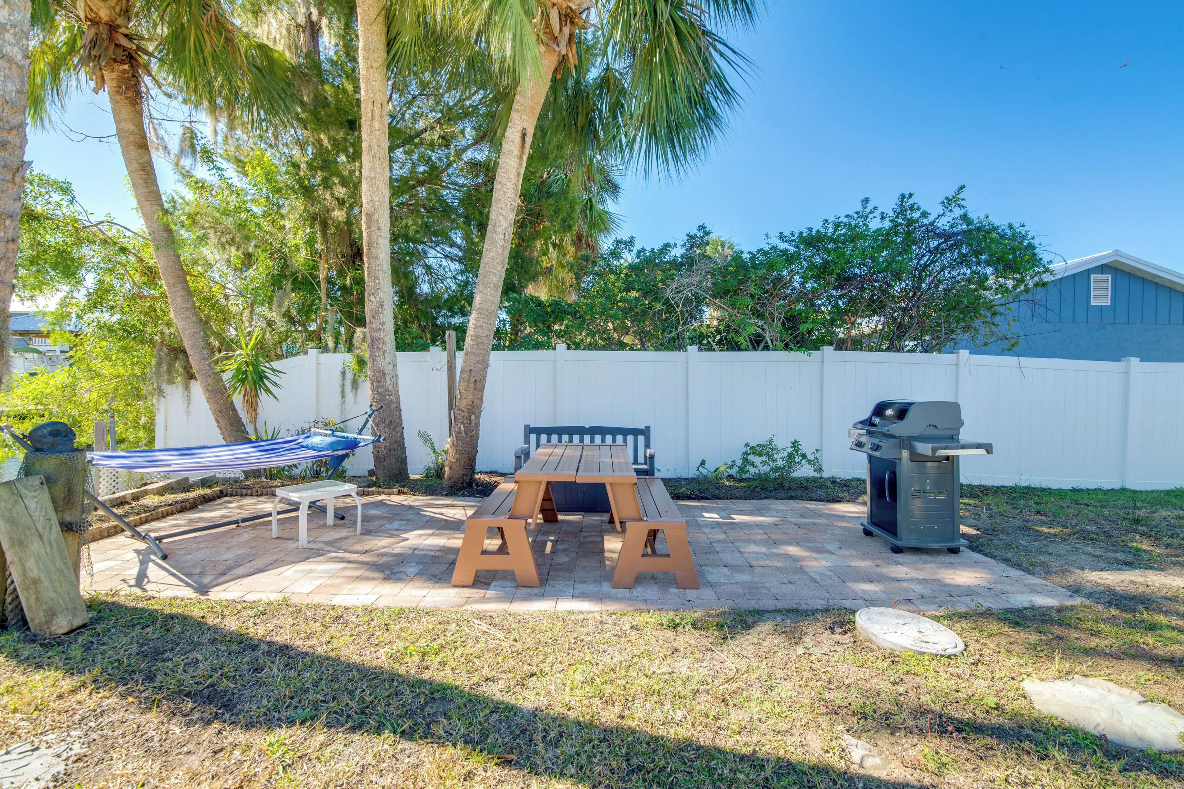 A backyard with a picnic table, a hammock, and a grill.