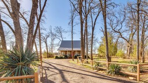 A building with a metal roof, surrounded by trees and a gravel path leading to a wooden fence. - Anglers' Haven! Cedar Creek Reservoir Getaway (Kemp)