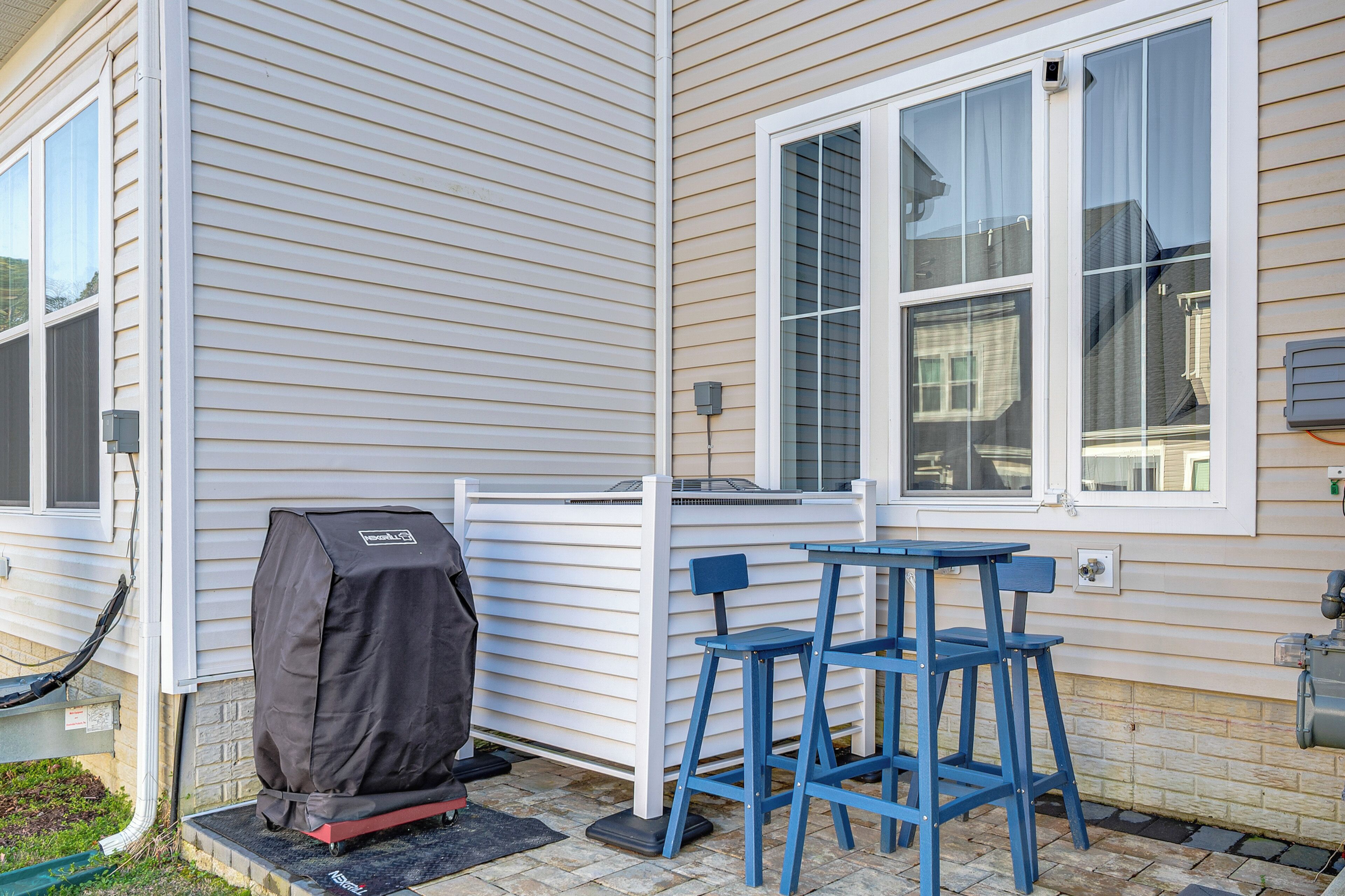 A house exterior with a covered grill, a white fence, and a blue outdoor table and chairs.