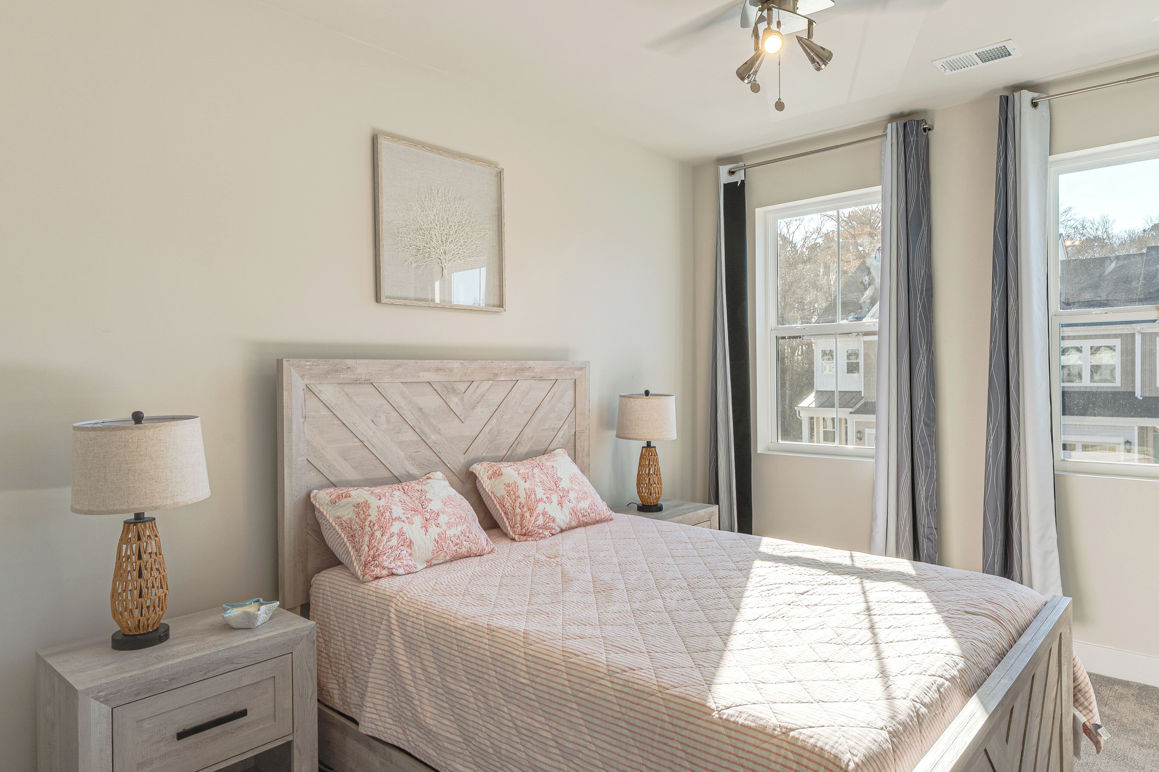 A bedroom with a large bed, two bedside tables, a nightstand, a ceiling fan, and a window with curtains.