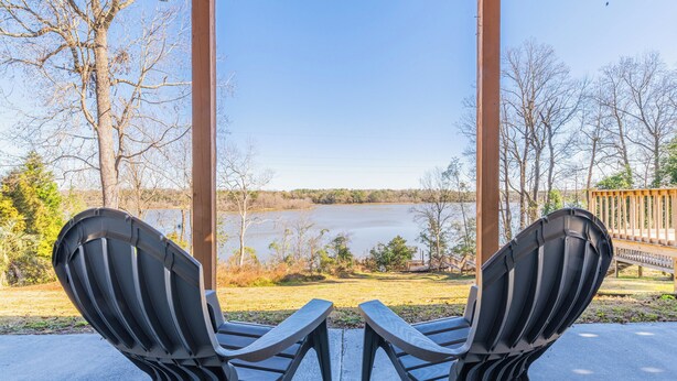 Deux chaises Adirondack sont placées face à un lac, avec une terrasse en bois et une rambarde en bois en arrière-plan.