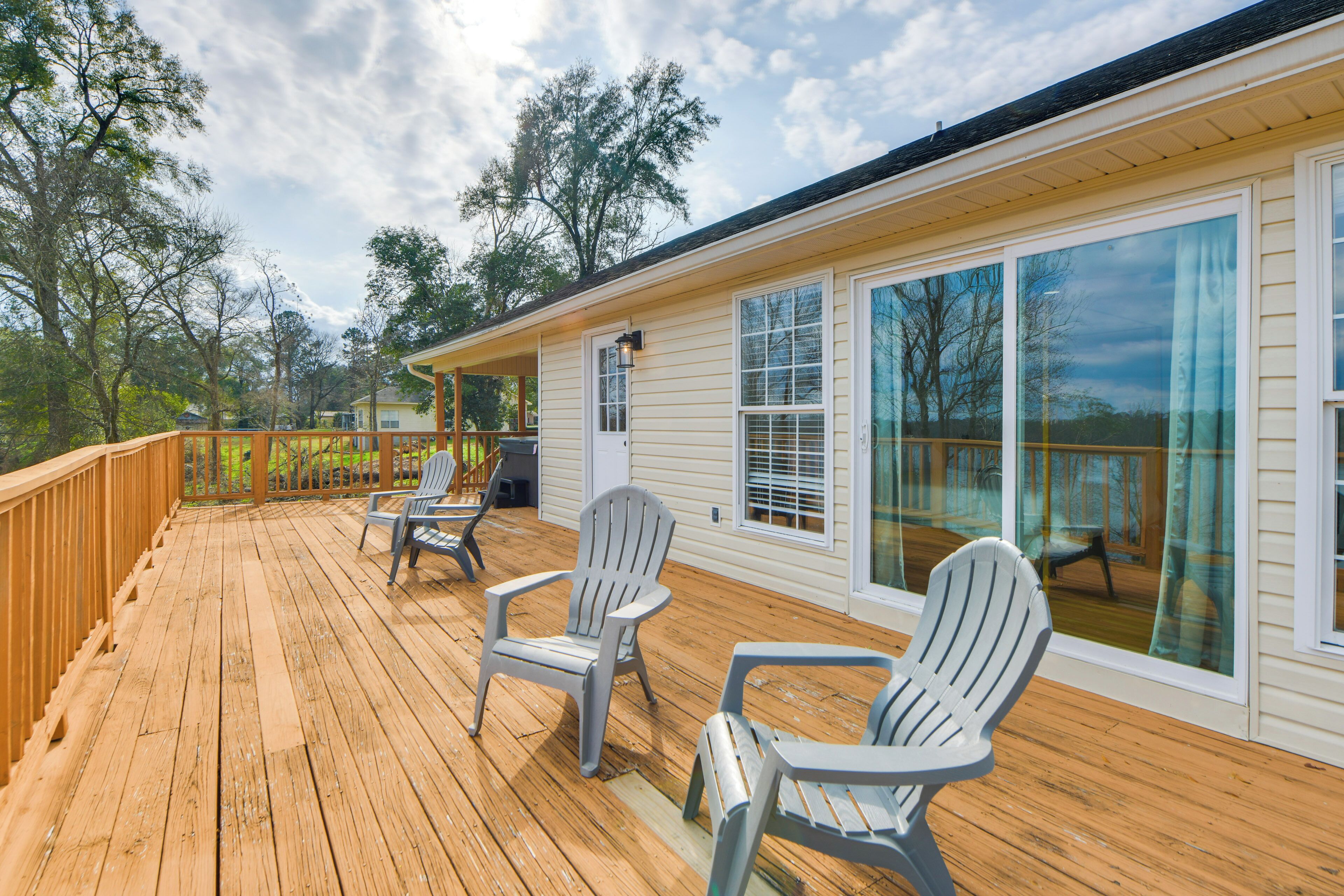 Eine Holzterrasse mit Adirondack-Stühlen, großen Fenstern und Blick auf Bäume.