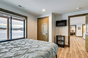 Un dormitorio con una cama grande, una puerta corrediza de vidrio, televisión y vistas a un paisaje nevado.