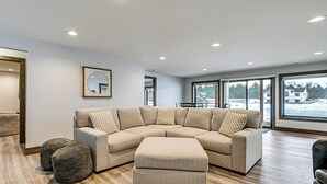 Un salon moderne avec un canapé d’angle, un pouf et un grand miroir au mur.