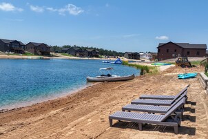 Una propiedad frente al lago con playa de arena, sillas de descanso, un muelle con barcos y un edificio grande.