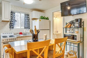 A compact kitchen with a stove, sink, and microwave. There is a dining table with chairs and a TV mounted above it. - Walkable Delphi Studio on Main Street w/ Parking (Delphi)