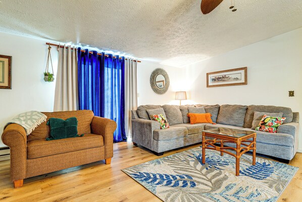 A living room with a brown armchair, a grey sofa, and a glass coffee table.