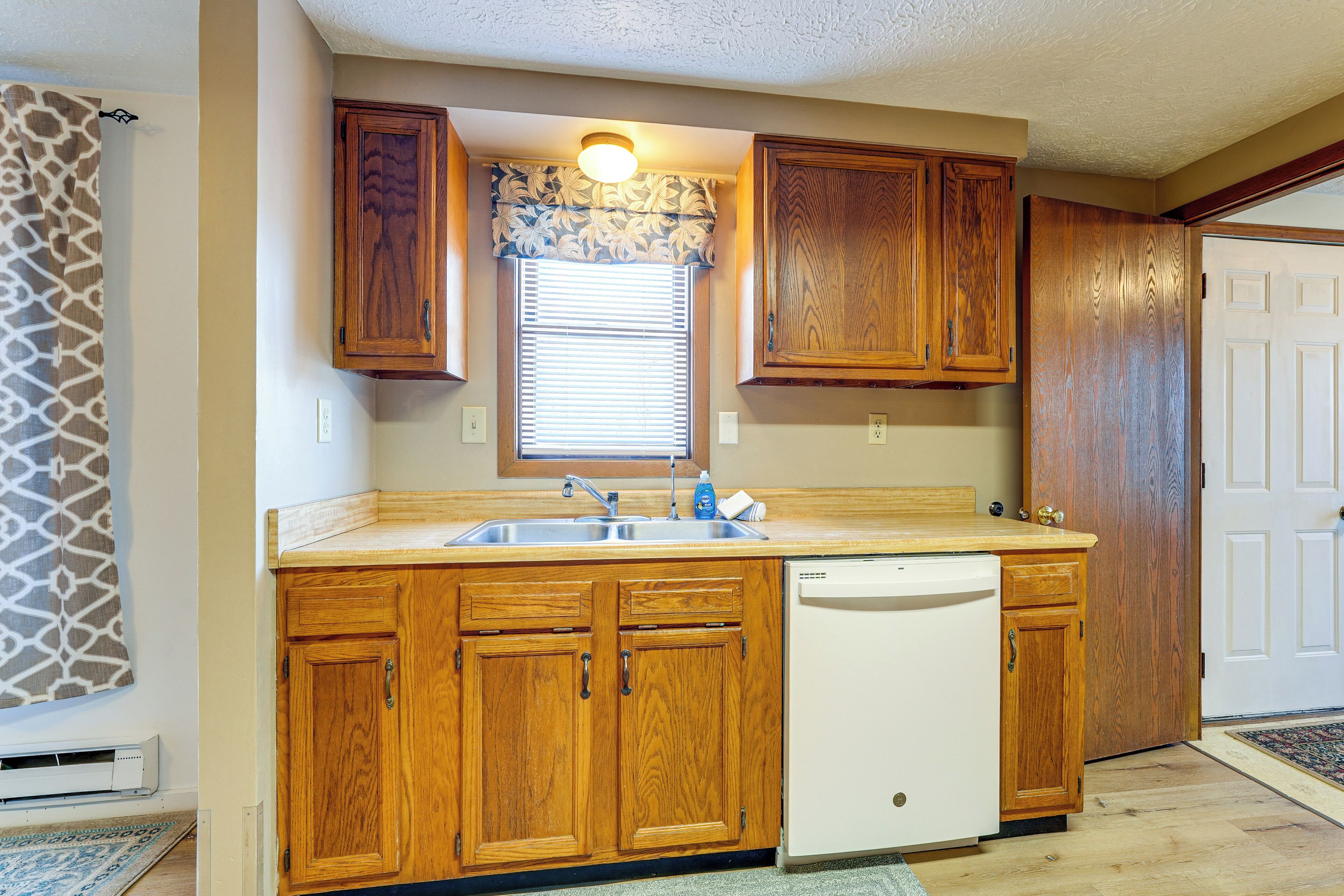 A kitchen with wooden cabinets, a built-in dishwasher, and a window with blinds.