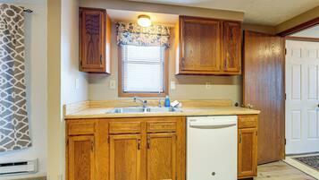A kitchen with wooden cabinets, a built-in dishwasher, and a window with blinds.