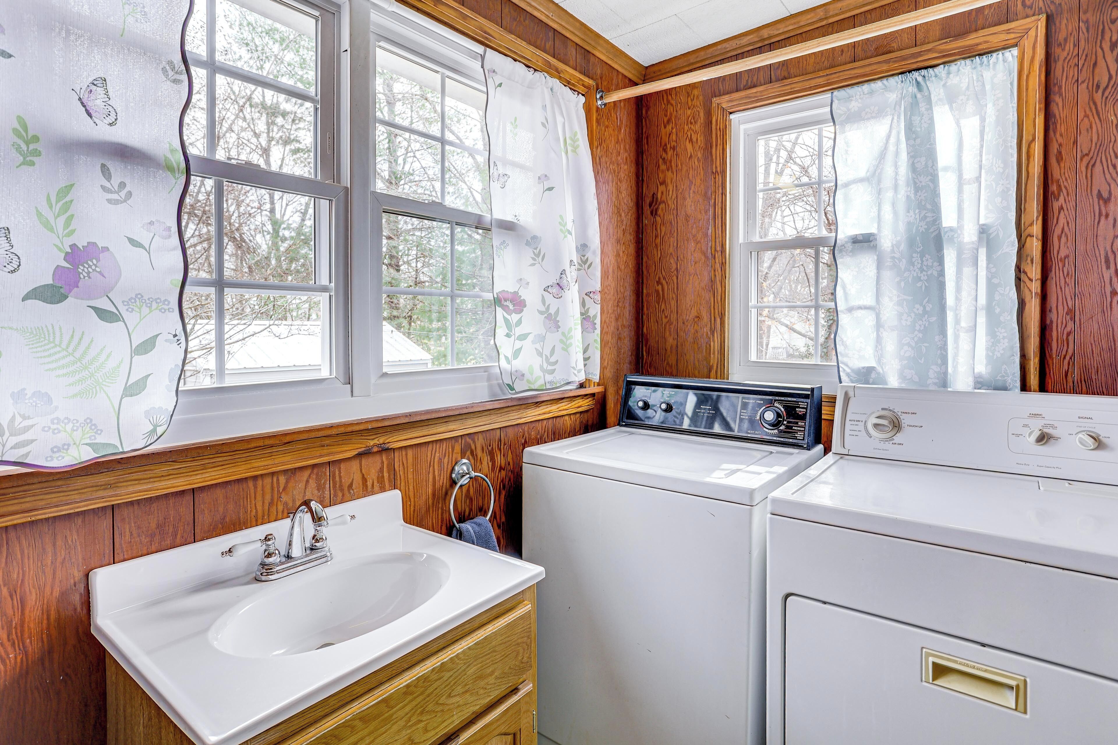 A laundry room with a sink, two washing machines, and wooden walls.