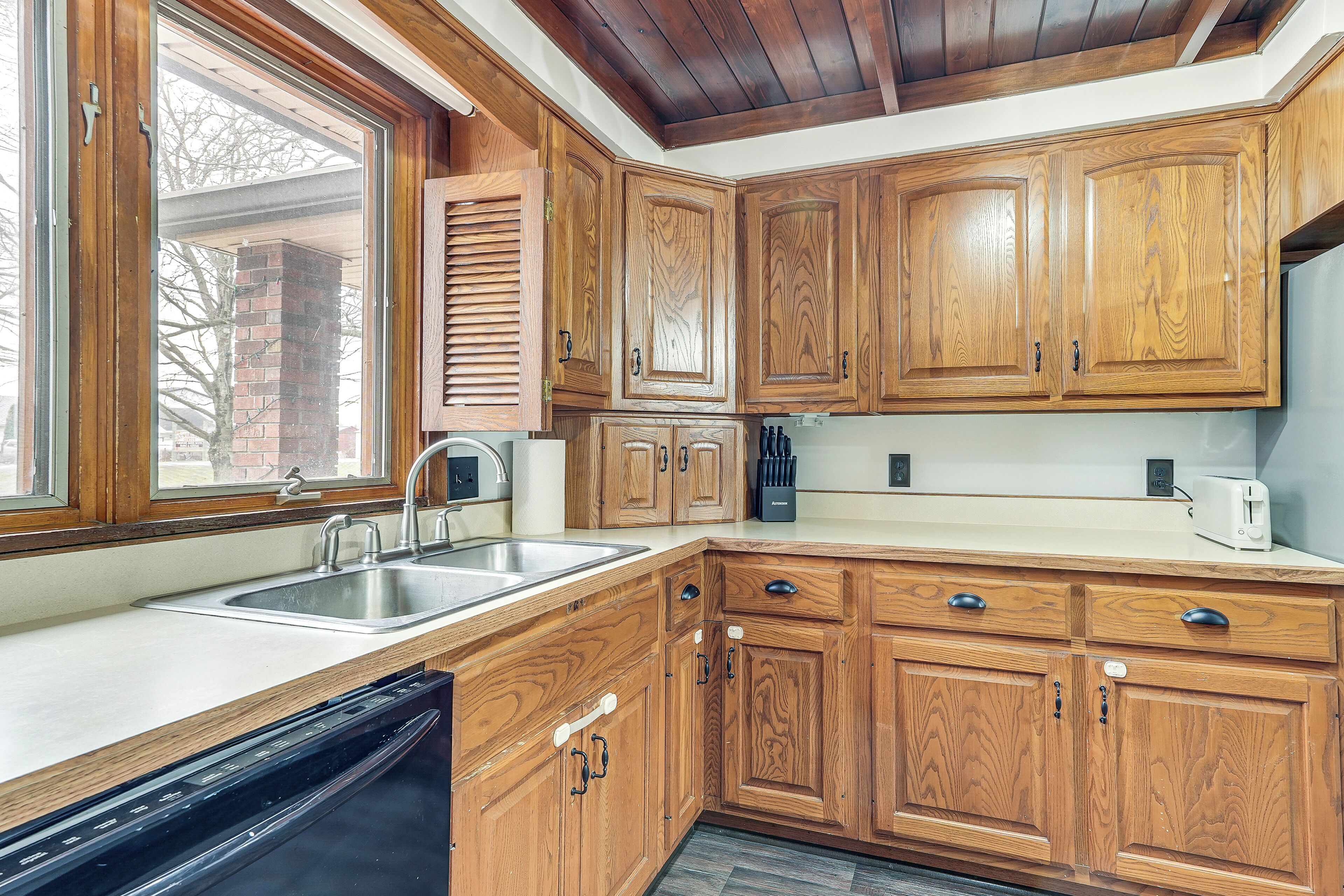 A kitchen with wooden cabinets, a dishwasher, and a window with blinds.