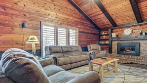 A cozy living room with a fireplace, wooden walls, and a sofa. - Woodburn Group Getaway: Endless On-site Fun! (Harlan)