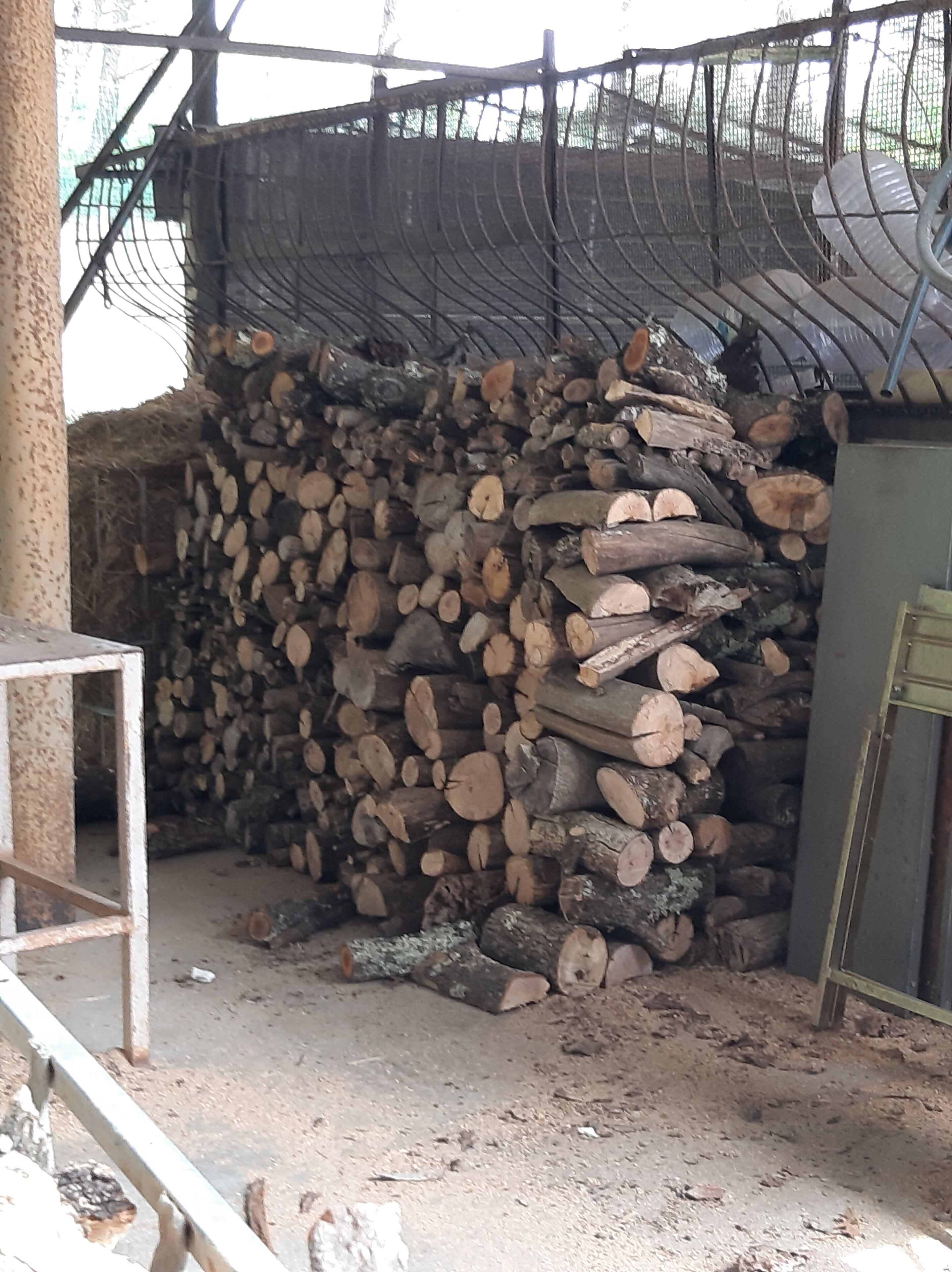 Una pila de leña en un área de almacenamiento con una cerca metálica y suelo de concreto.
